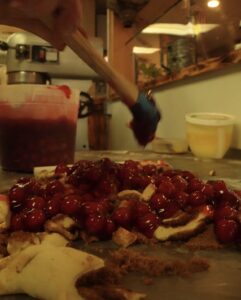 A cherry fritter with a bright red pile of fruit getting mixed in