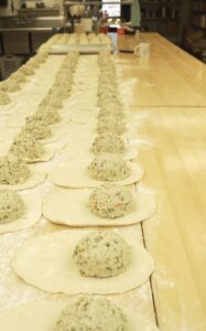 Rows of uncooked simply baked dumplings on a wooden countertop in a kitchen, with neatly placed dough and vegetable filling, creating a sense of preparation and focus.