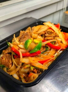 Thai by Tom black takeout container filled with stir-fried noodles, beef slices, red and green bell peppers, onions, and spices, creating a vibrant, appetizing look.