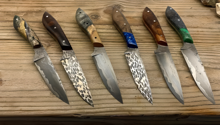 Six handcrafted Silver Anvil Metalcraft knives with unique, patterned blades and colorful handles are displayed on a wooden surface, showcasing intricate craftsmanship.