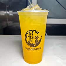 A vibrant yellow Bobablastic iced fruit tea served in a clear plastic cup on a counter.