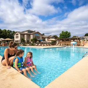 Two children in swim vests at the edge of a resort pool while a parent watches