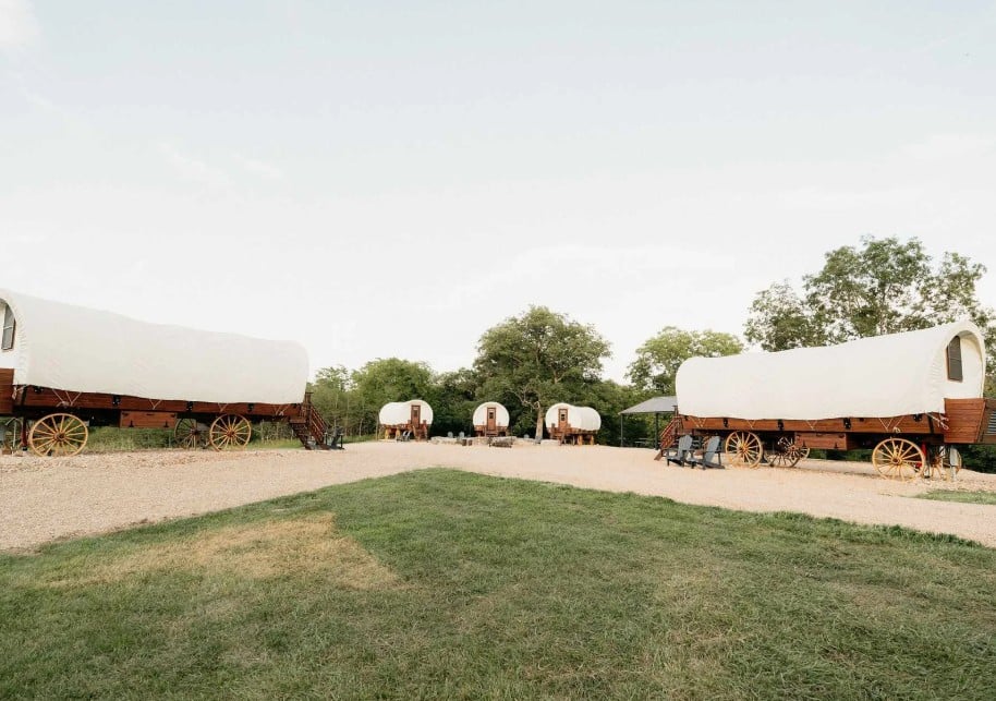 White-topped covered glamping wagons across a grassy field at the Private 6-Wagon Ranch in Branson