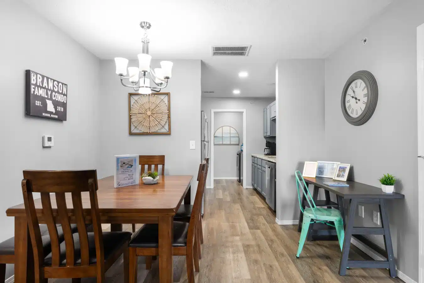 Dining table under a chandelier next to a galley kitchen with a stainless steel refrigerator at Side by Side Spacious Condos in Branson