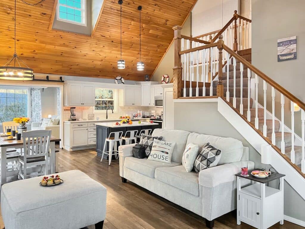Open great room with a vaulted wood ceiling, white kitchen and staircase at Cozy Home with private hot tub near Silver Dollar City in Branson