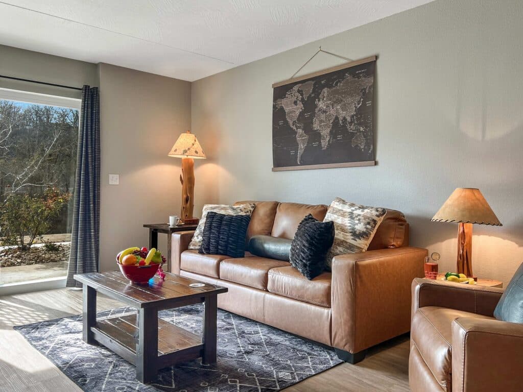 Living room with a leather sofa, rustic lamps and a sliding door to a wooded patio at Upscale Condo, Walk to Branson Landing in Branson